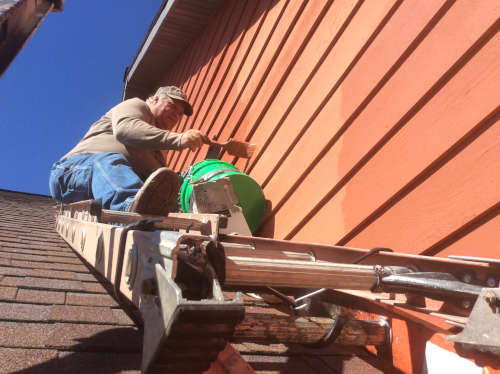 A close-up shot of Scott using a ladder secured to the roof in order to safely work this dangerous spot.